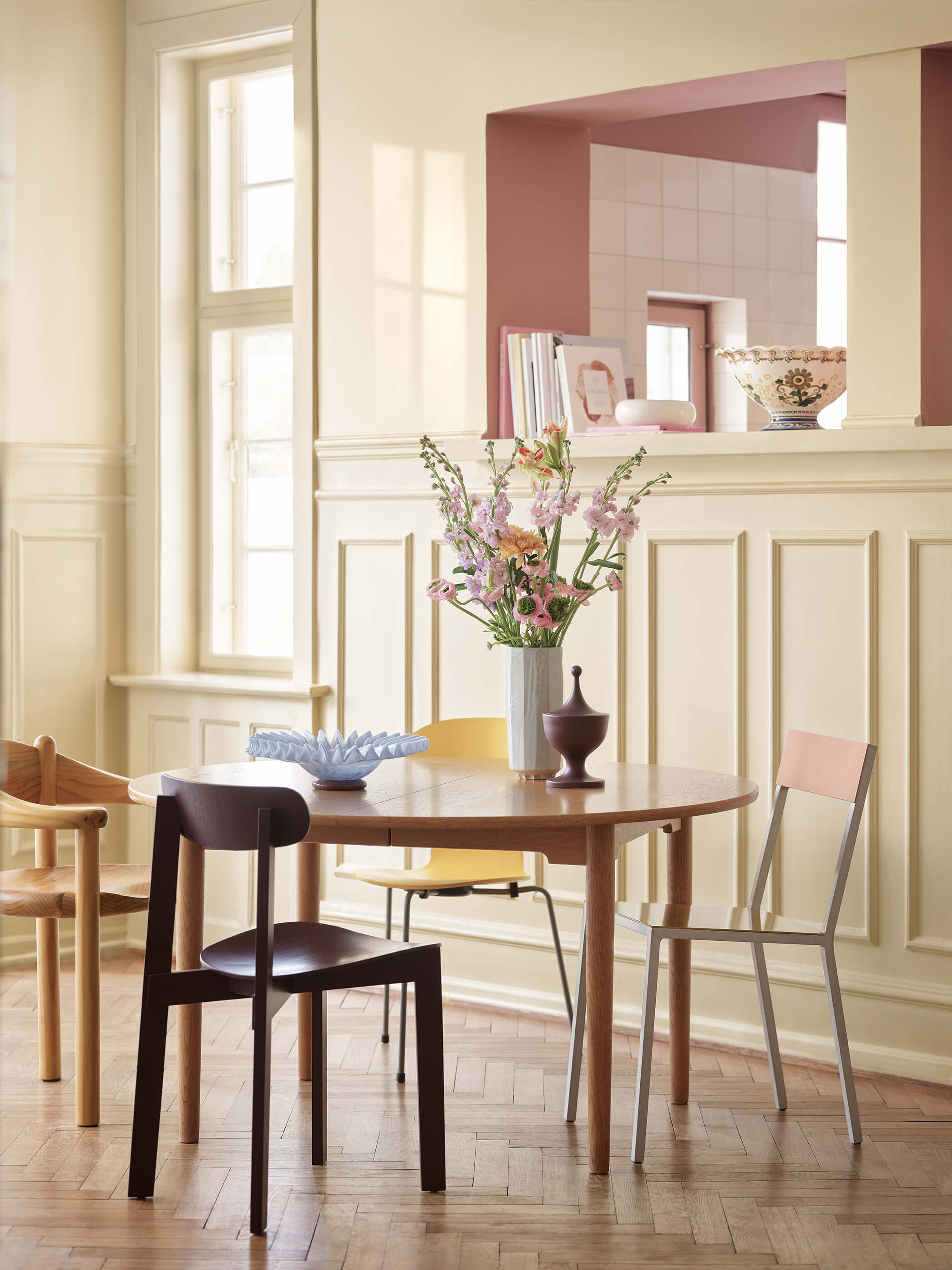 Kjøkken med vegger malt lyst gule med Jotun 11365 Morning Glow og rosa Jotun 20256 Balmy Pink på den innfelte veggen. Et spisestuesett i tre står plassert i midten