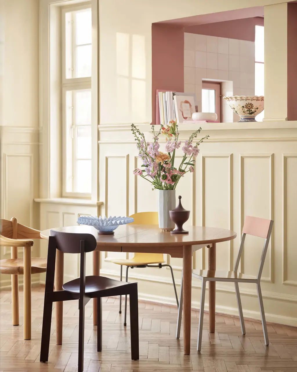 Kjøkken med vegger malt lyst gule med Jotun 11365 Morning Glow og rosa Jotun 20256 Balmy Pink på den innfelte veggen. Et spisestuesett i tre står plassert i midten