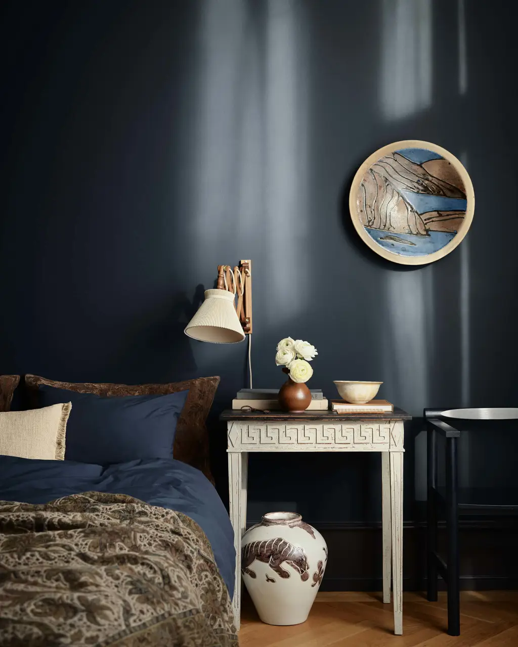 Et stemningsfullt soverom med dyp marineblå vegger i Jotun 4403 Midnight Blue, et vintagehvitt nattbord, en vegglampe og matchende blått sengetøy