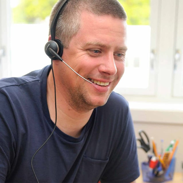 Person med headset som arbeider ved skrivebord i et lyst kontormiljø.