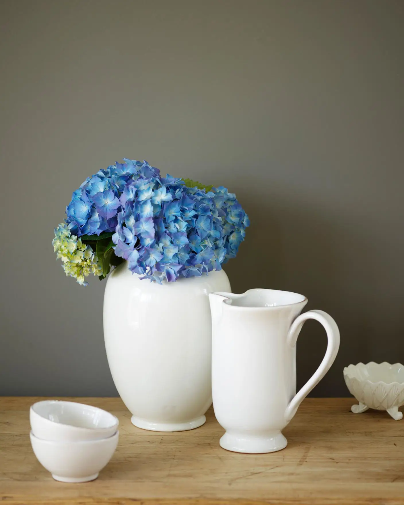 Vit keramik och klara blå blommor mot en vägg målad med 1462 Grå Skiffer, en gyllengrå färg från Jotun. Naturligt trä tillför värme och håller helheten lugn och harmonisk.