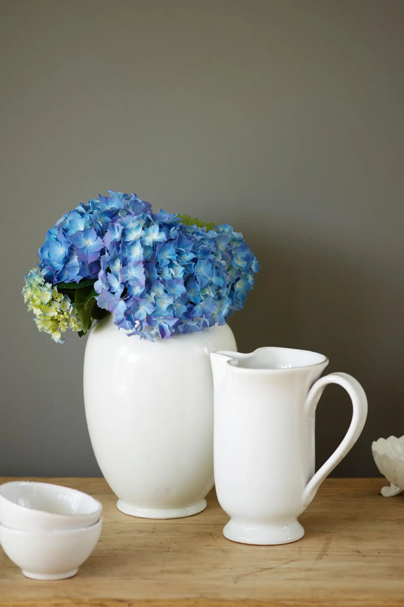 Cerámicas blancas y flores azul brillante frente a una pared pintada con Jotun 1462 Evening Sky, un color gris dorado. La madera natural aporta calidez y mantiene el conjunto tranquilo y equilibrado.