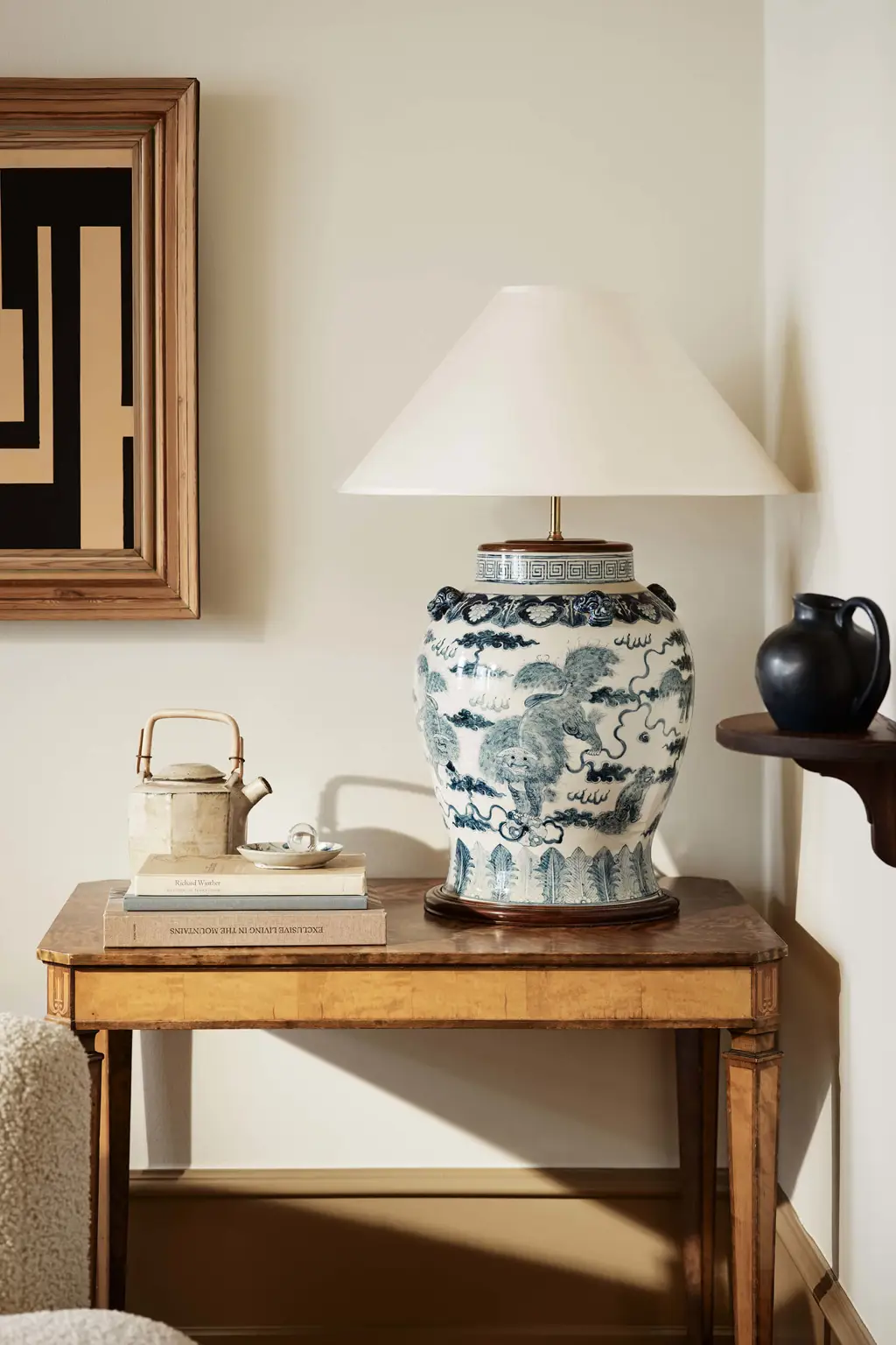 En stue med vægge i Jotun 1281 Perlebeige og lister malet i Jotun 1799 Spice Brown, indrettet med et bord og en blå og hvid keramisk lampe.