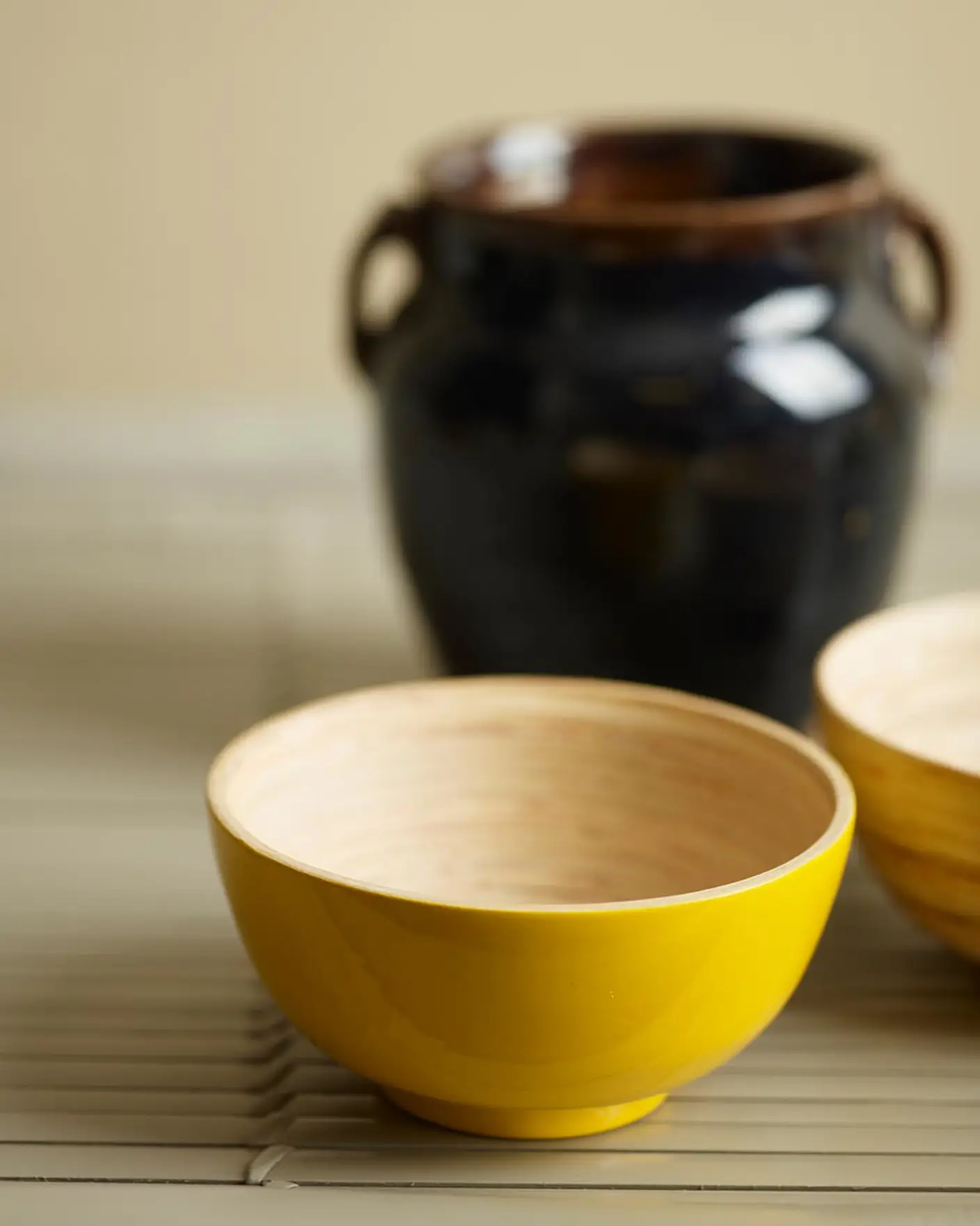 A yellow bowl and ceramics on a pale olive surface with a background painted with 10343 Lush Oasis, a muted, brownish yellow colour from Jotun.