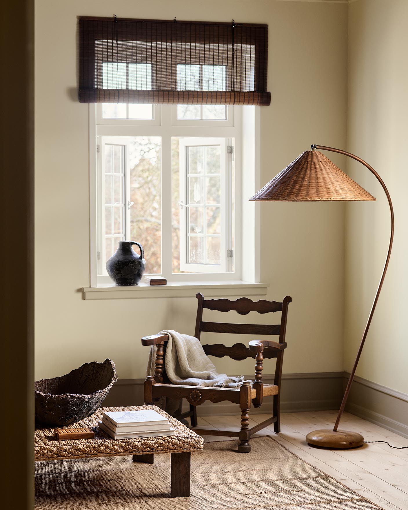 A wooden chair, woven lamp, and coffee table against a muted yellow wall painted in the colour 12080 Soft Radiance from Jotun.