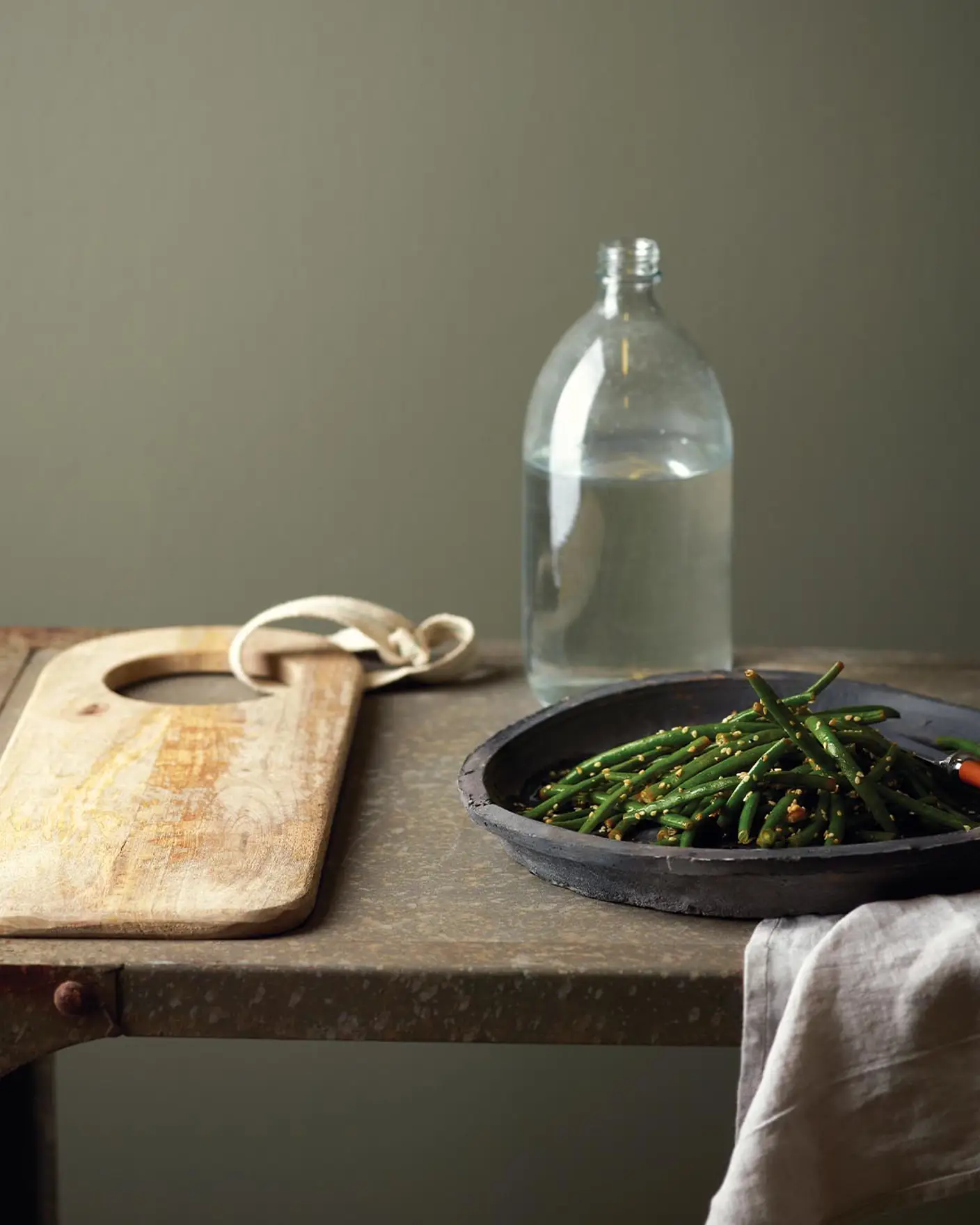 Gröna bönor serveras i en rustik svart skål på ett väderbitet metallbord, mot en mörk, dämpad grön vägg målad med Jotun 8304 Timjan.
