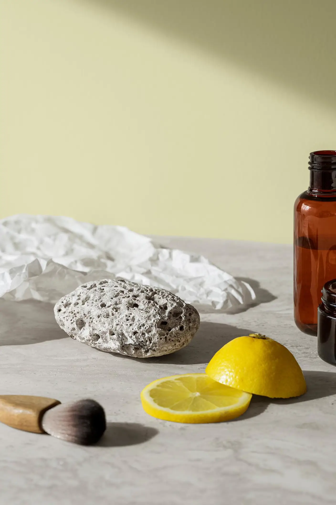 En pimpsten, hudvårdsburkar och citronskivor vilar på en marmoryta och skapar en fräsch och ren känsla mot en mjuk gulgrön bakgrund målad med färgen 8087 Vårluft från Jotun.