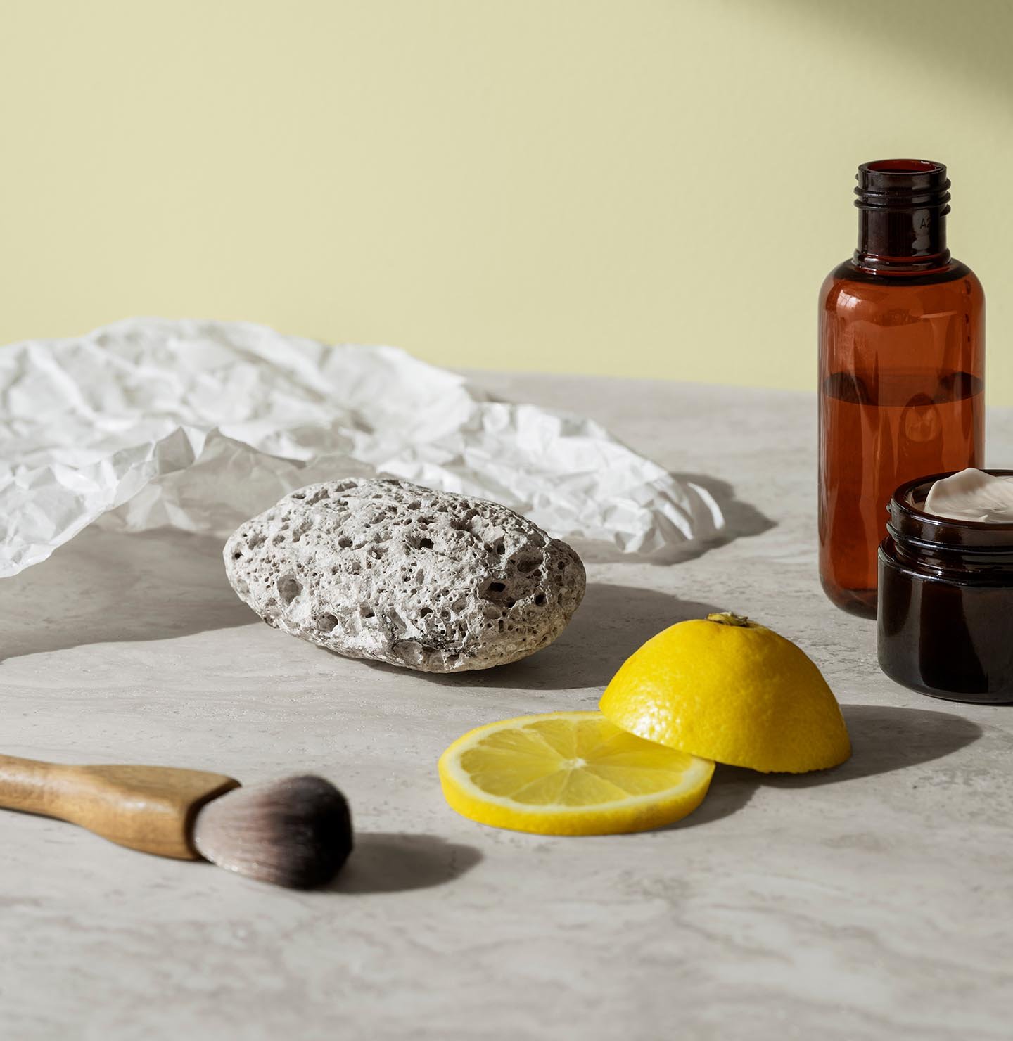 En pimpsten, hudvårdsburkar och citronskivor vilar på en marmoryta och skapar en fräsch och ren känsla mot en mjuk gulgrön bakgrund målad med färgen 8087 Vårluft från Jotun.