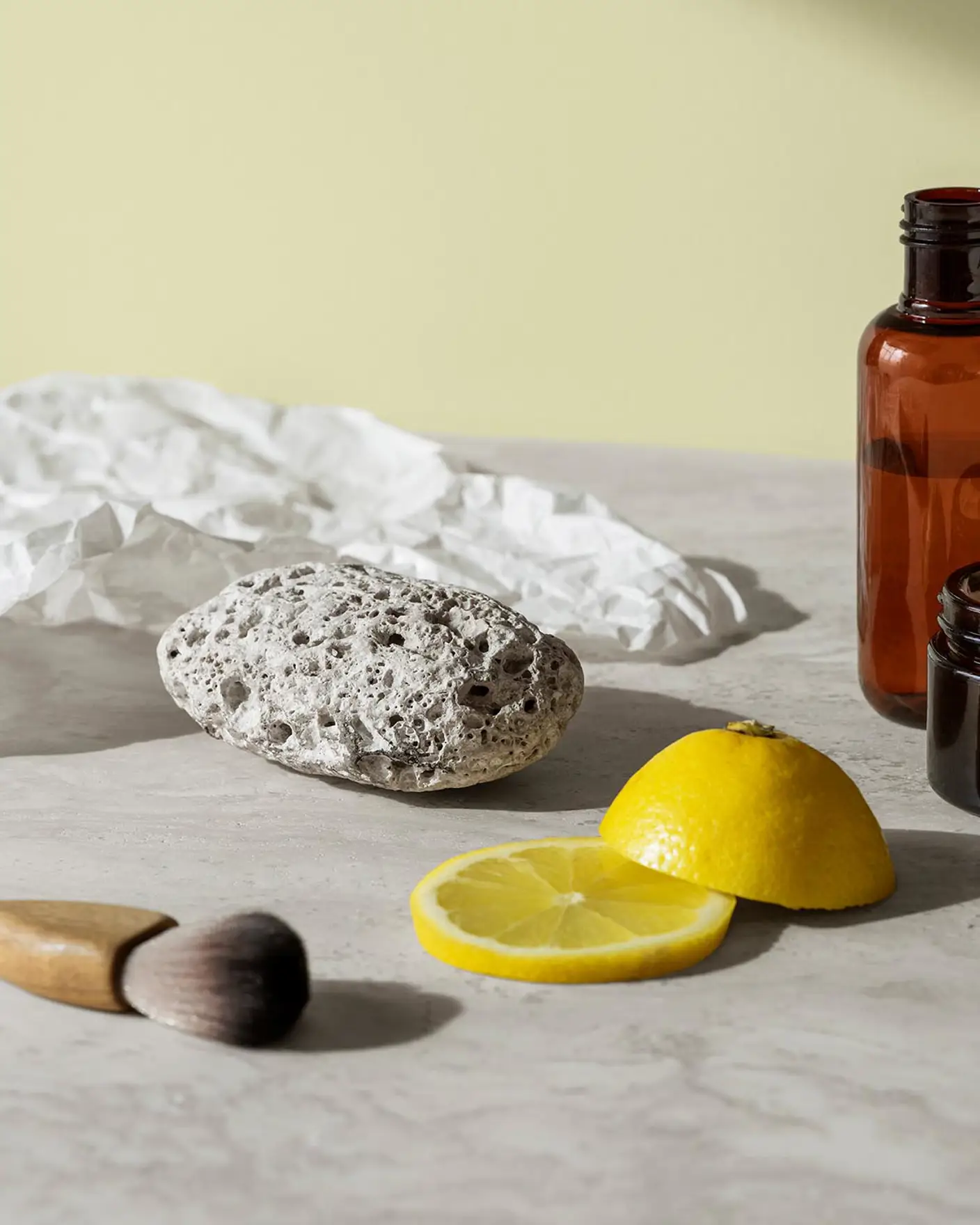 En pimpsten, hudvårdsburkar och citronskivor vilar på en marmoryta och skapar en fräsch och ren känsla mot en mjuk gulgrön bakgrund målad med färgen 8087 Vårluft från Jotun.