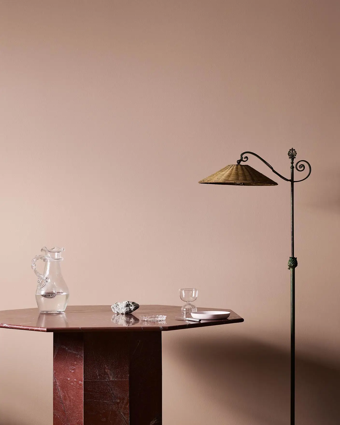 A red marble table, glassware, and floor lamp against a soft pink wall painted in the colour 20362 Pink Ambience from Jotun.