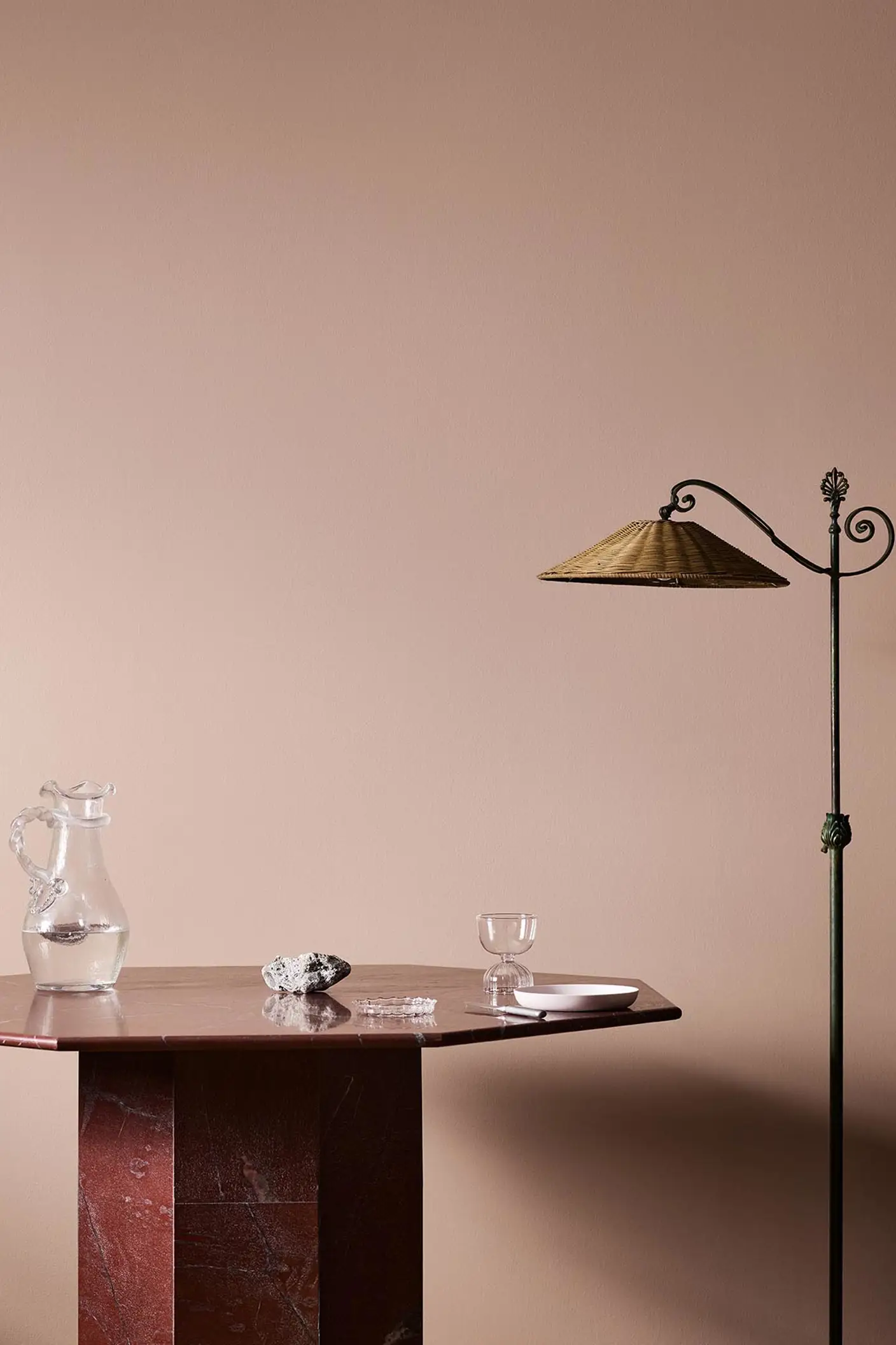 A red marble table, glassware, and floor lamp against a soft pink wall painted in the colour 20362 Pink Ambience from Jotun.