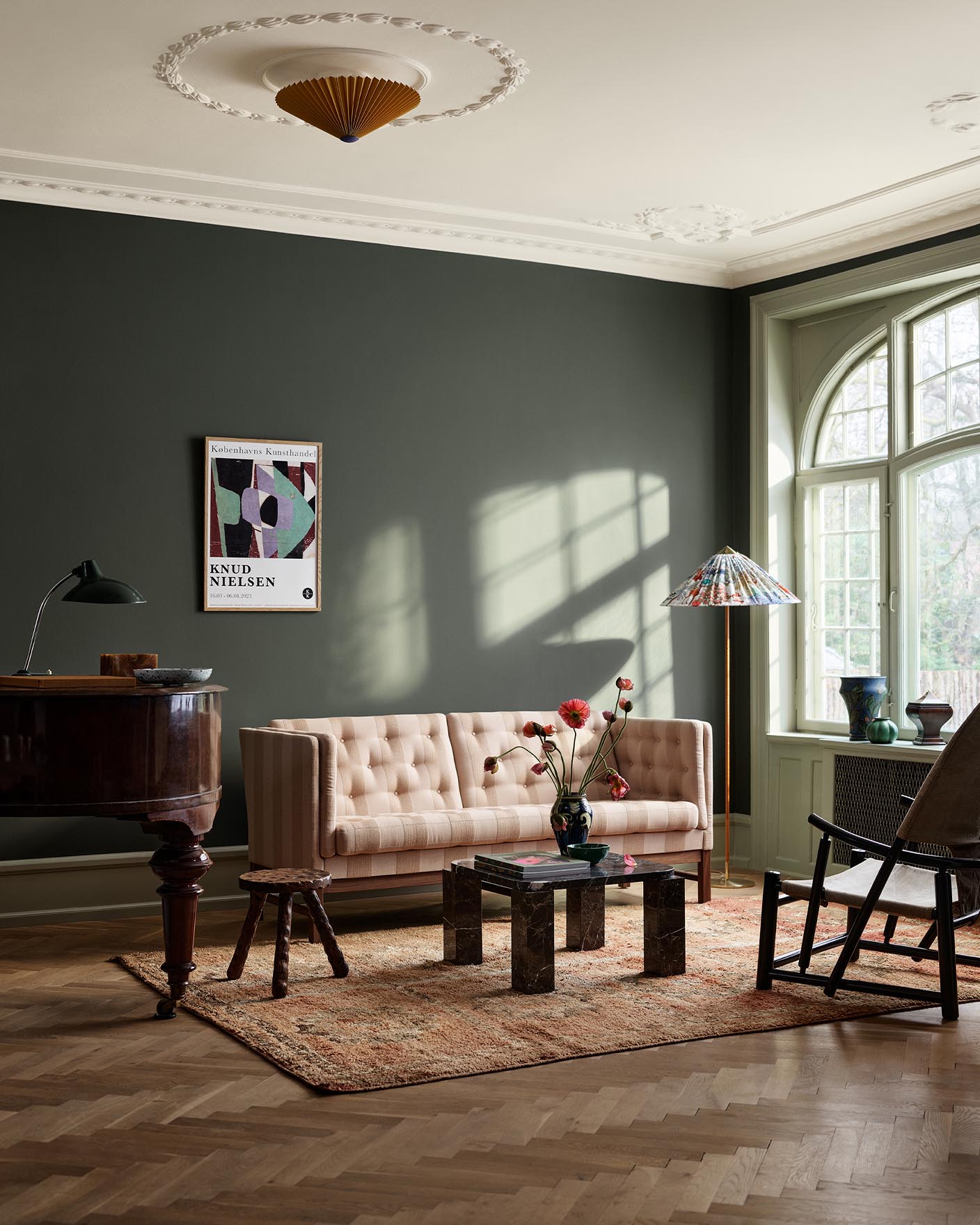Living room with beige sofa, wooden table, and decor against a dark, muted green wall painted with the colour Jotun 7613 Northern Mystic.
