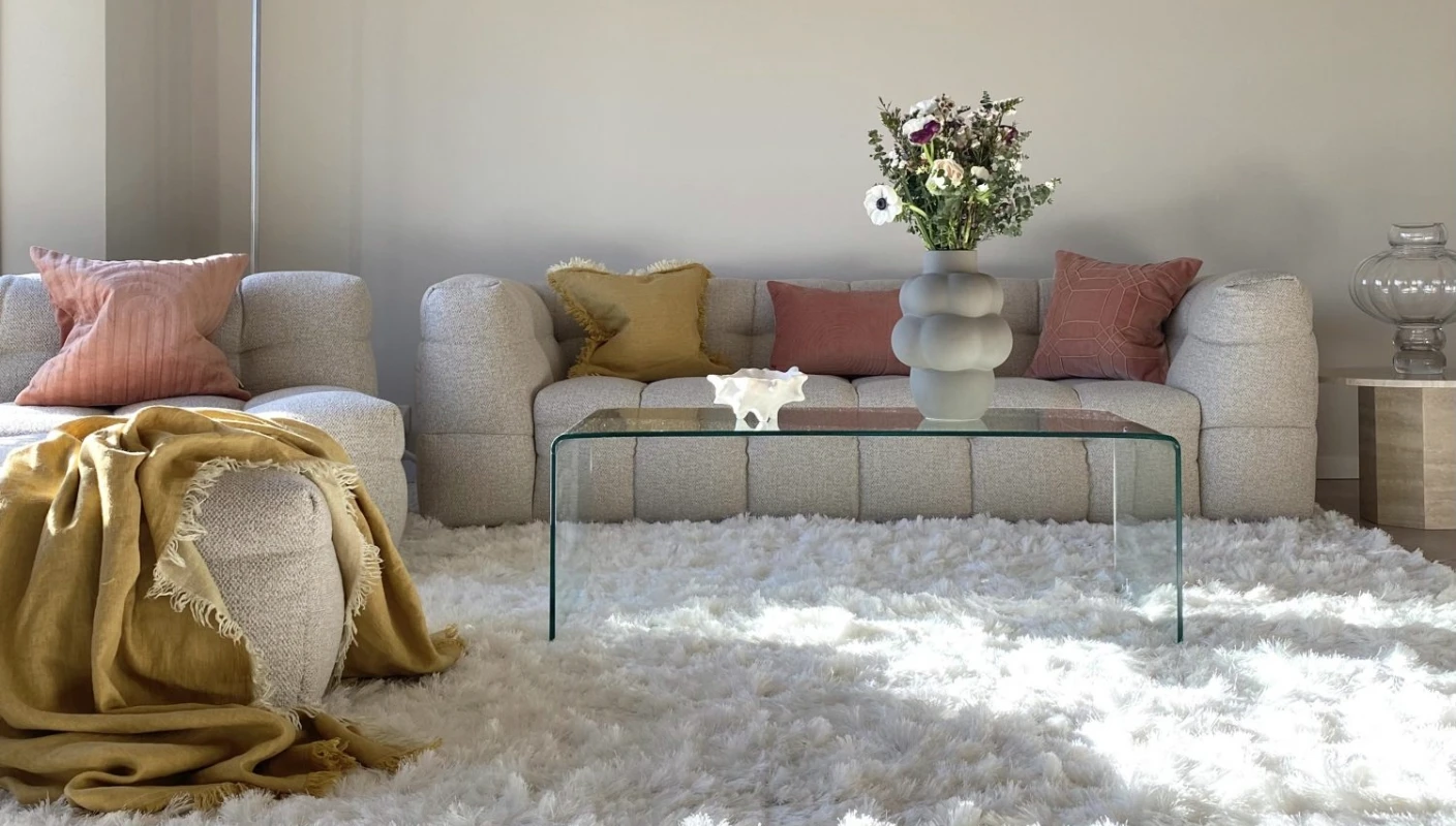 Moderne skandinavisk stue i Jotun Soft Skin. Beige sofa med rosa pynteputer og en nydelig blomsterbukket i en grå vase på glassbordet.