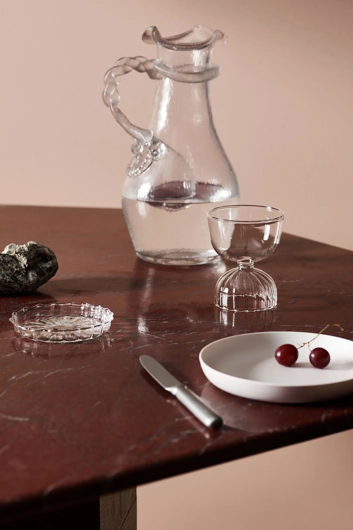 Glassware, cherries, and decor on a maroon marble table against a soft pink wall painted with the Jotun colour 20362 Pink Ambience.