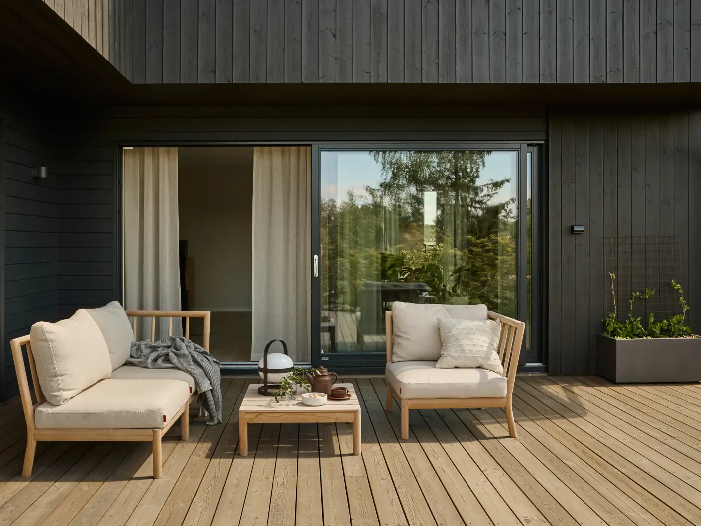 Terrasse møblert med beige utesofa og stol, terrassegulv beiset med TREBITT 9074 Nordisk Tre mot et moderne hus beiset i JOTUN 90033 Funkissort