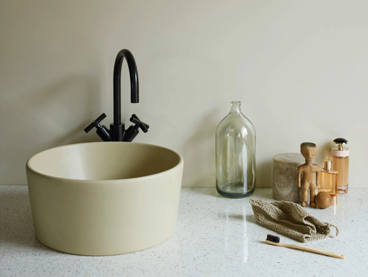 Moderne baderomsvask i beige med svart armatur, dekorative glassflasker og badeartikler på benkeplate