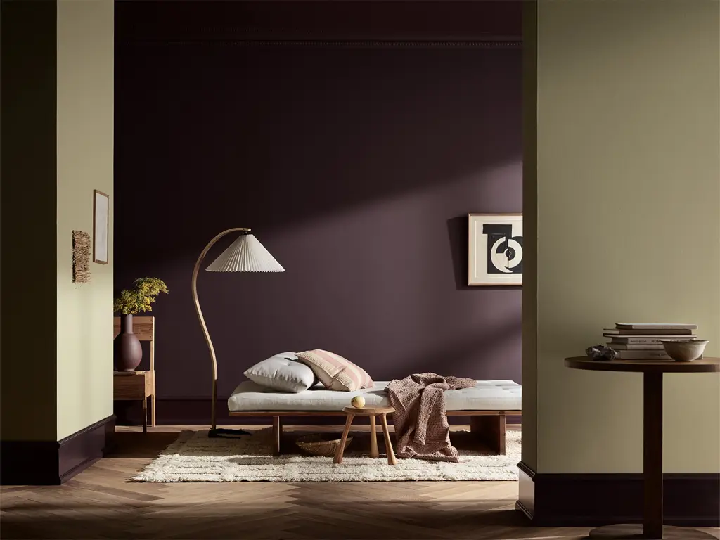 Stilfullt soverom med mørk lilla vegg i fargen Jotun Velvet Plum malt med LADY Pure Color, enkel seng, gulvlampe, småbord og moderne interiør