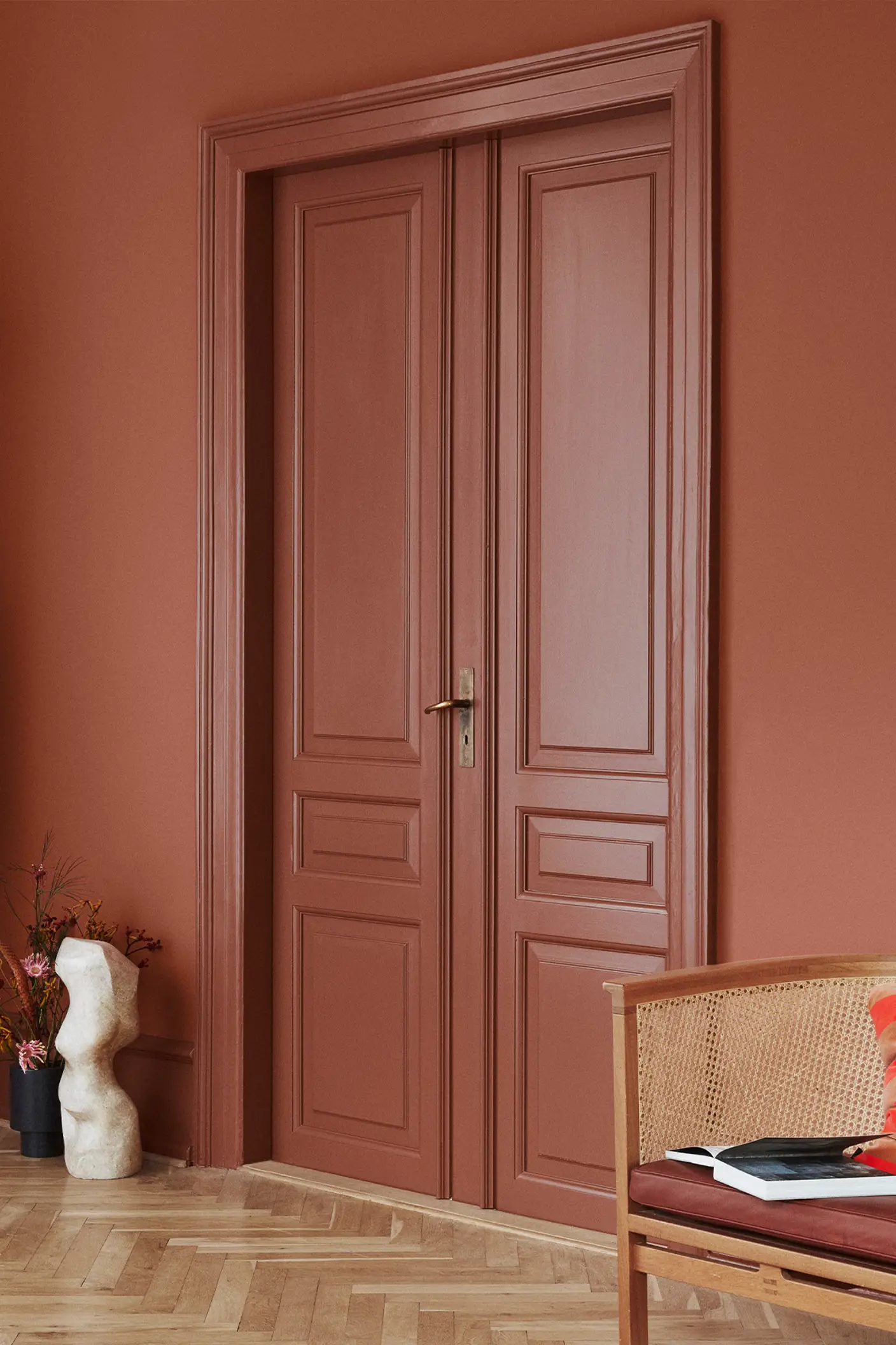 Double doors and walls painted in Jotun Lively Red, paired with Amber Red accents; rattan chair with red cushion and sculptural décor