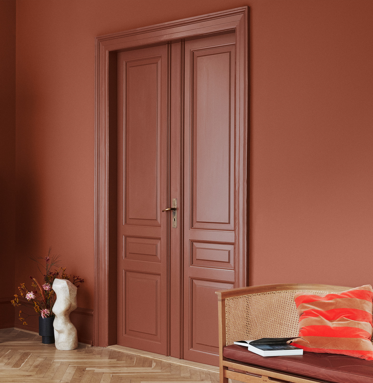 Dubbeldörrar och väggar målade i Jotun Lively Red, kombinerat med Amber Red-detaljer; rottingstol med röd dyna och skulptural dekor.