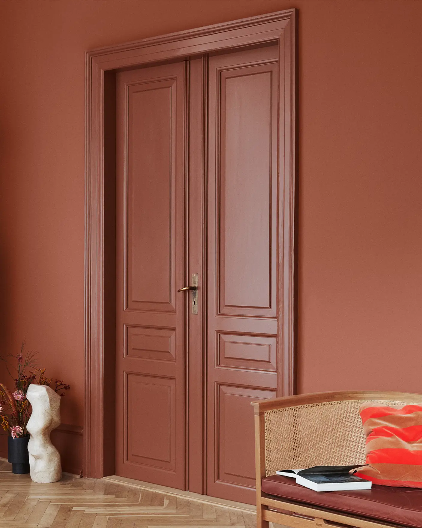 Dubbeldörrar och väggar målade i Jotun Lively Red, kombinerat med Amber Red-detaljer; rottingstol med röd dyna och skulptural dekor.