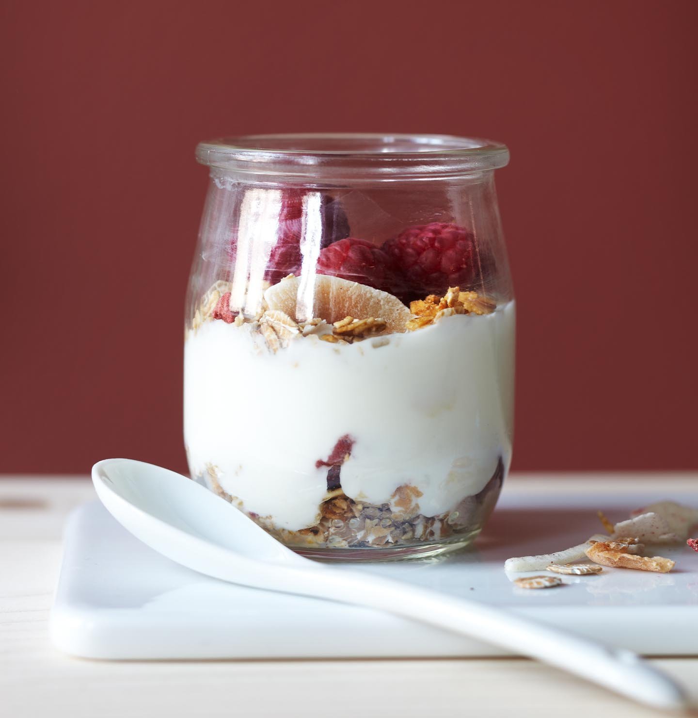 En djup röd vägg, målad i färgen 2859 Whispering Red från Jotun, tillför värme och djup till en enkel frukost med yoghurt, granola och bär.