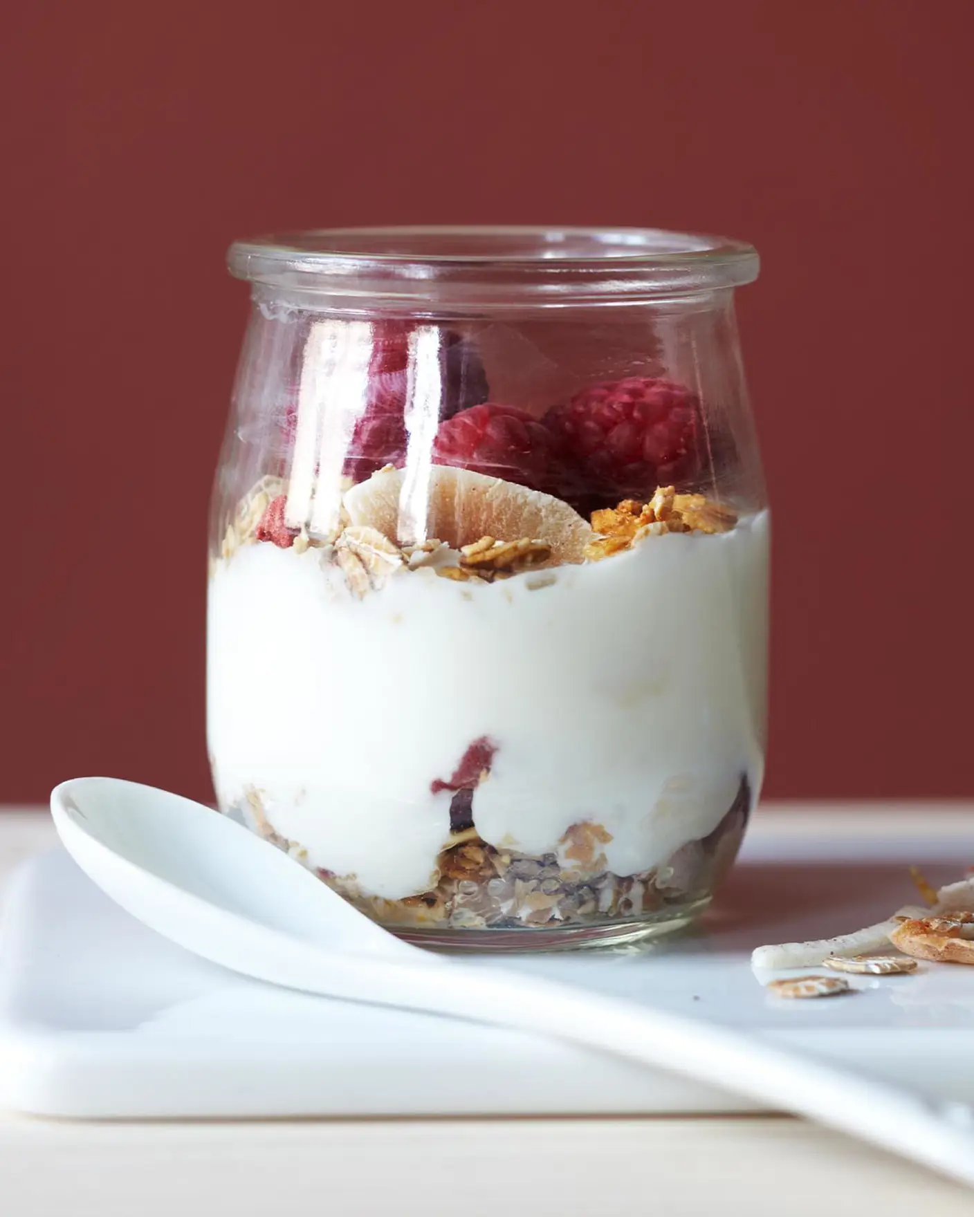 En djup röd vägg, målad i färgen 2859 Whispering Red från Jotun, tillför värme och djup till en enkel frukost med yoghurt, granola och bär.