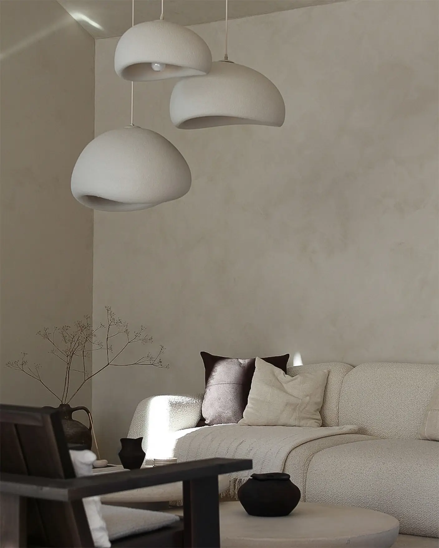 Lyst stuehjørne med beige sofa, mørke puter og organiske lamper i hvitt mot en kalkmalt vegg malt i fargen Jotun Sand