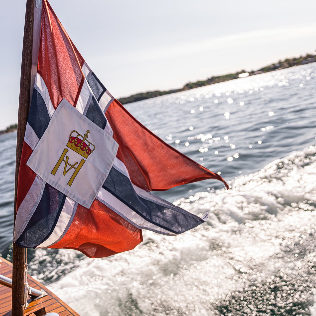 Båt i fart på sjøen med norsk flagg og skummende kjølvann