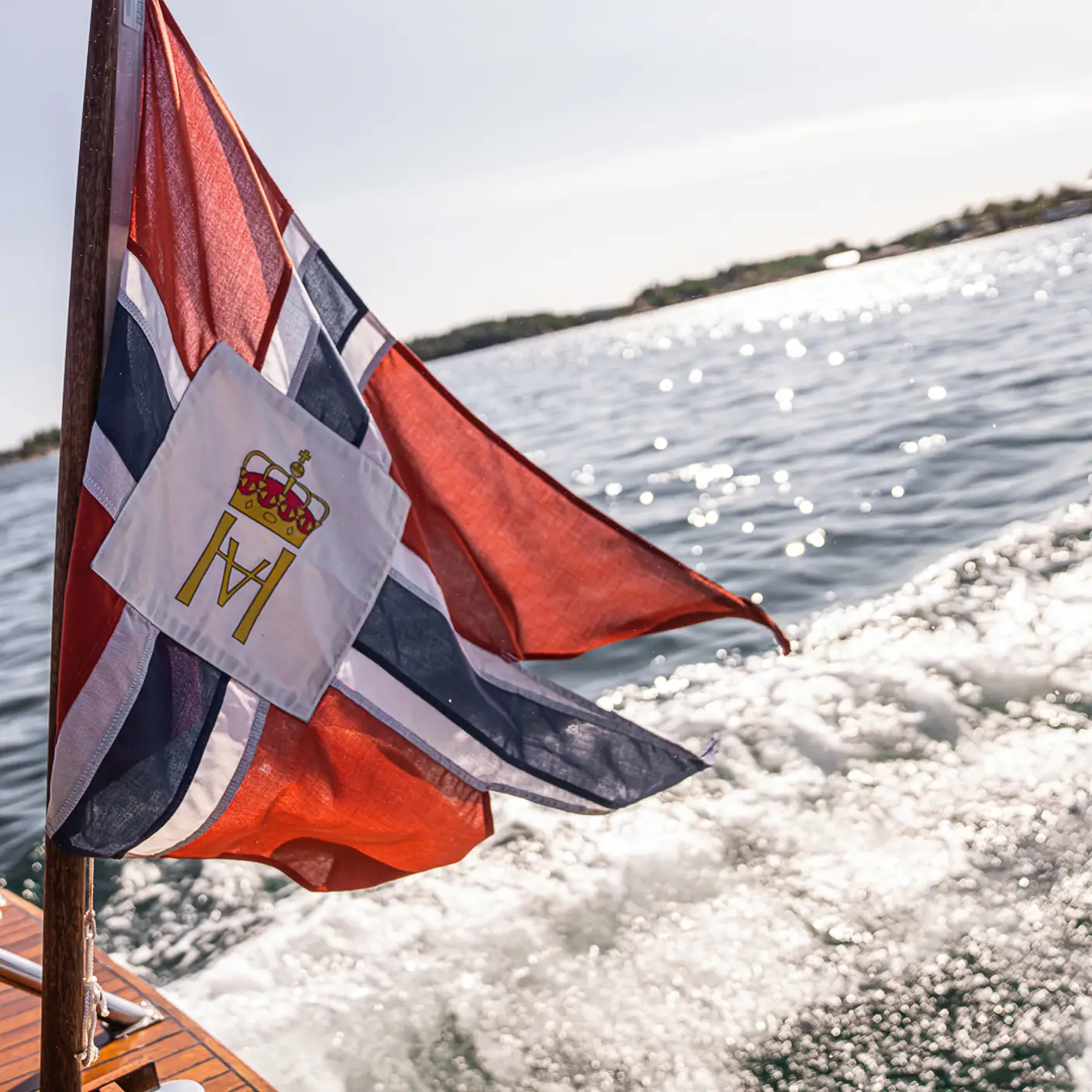 Båt i fart på sjøen med norsk flagg og skummende kjølvann