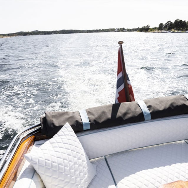 Båt i fart på sjøen med norsk flagg og lyse puter på akterdekket