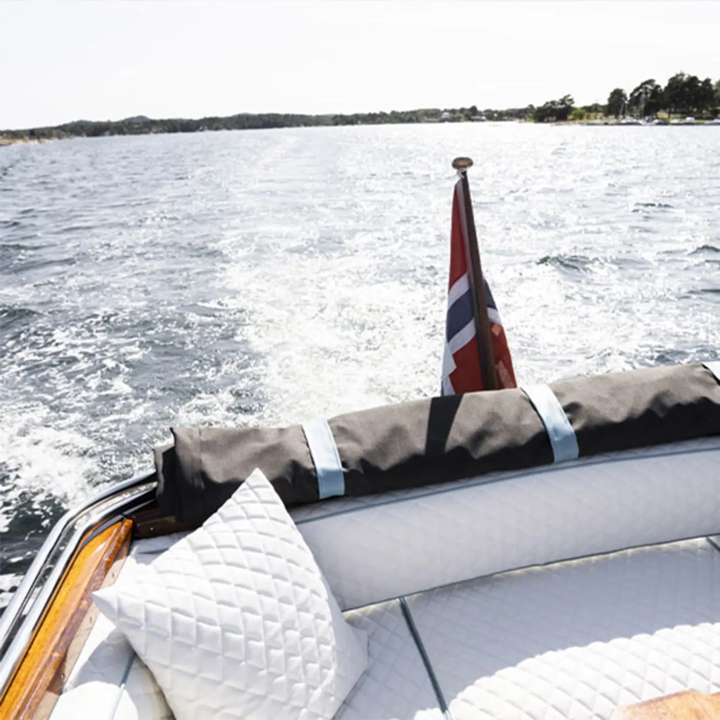 Båt i fart på sjøen med norsk flagg og lyse puter på akterdekket