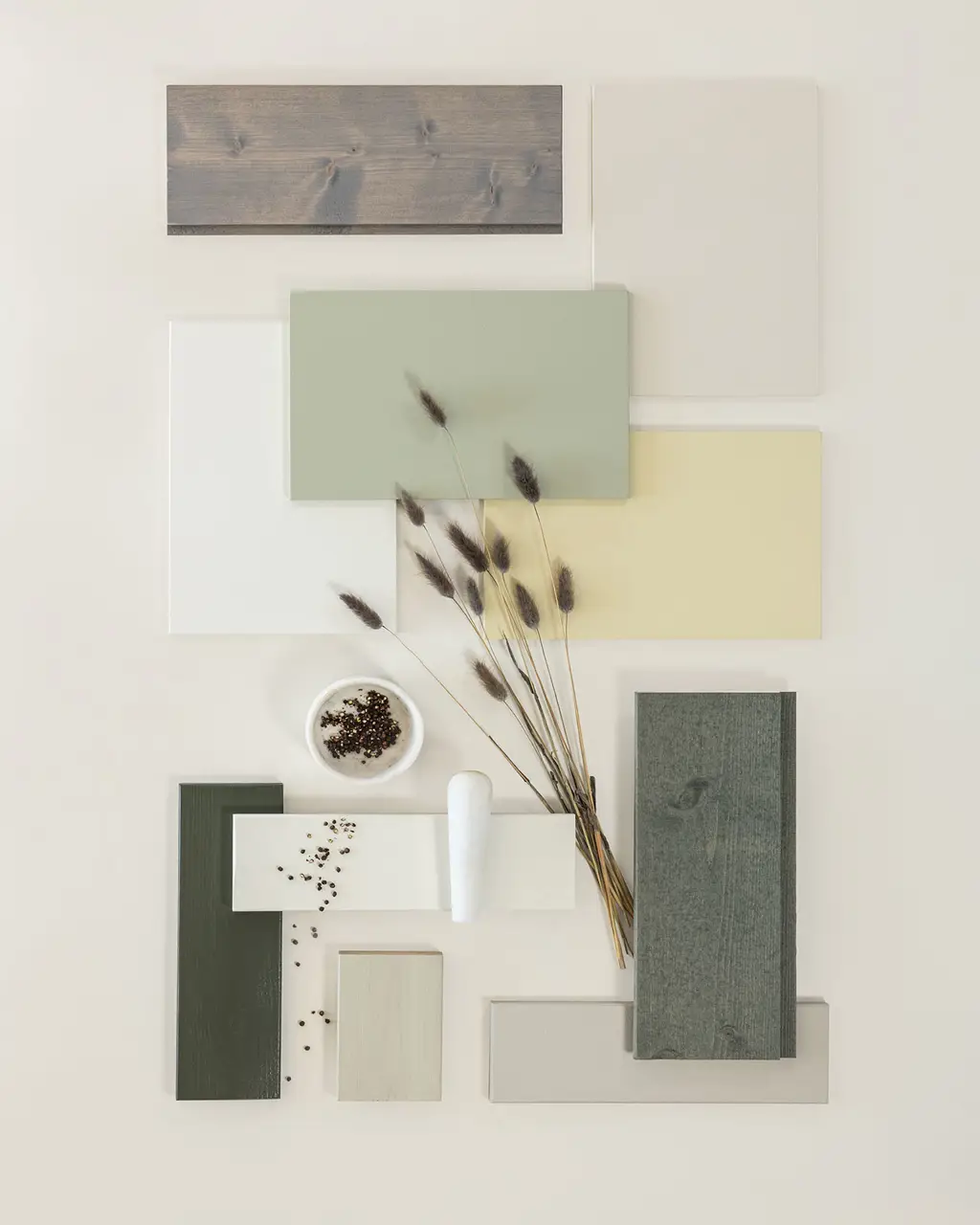 Färgprover i jordtoner, inklusive grönt, beige och trästruktur, arrangerade med dekorativa frön och torkade stjälkar på en ljus bakgrund.