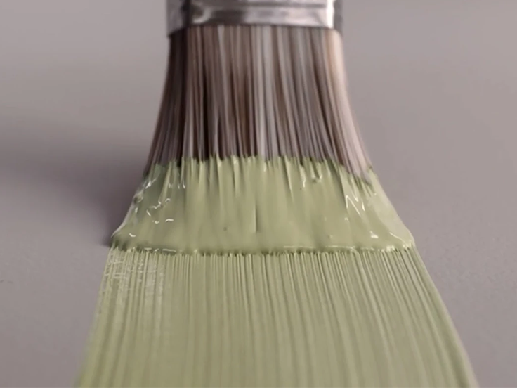 Pensel med ljusgrön färg stryker färgen över en grålila yta.