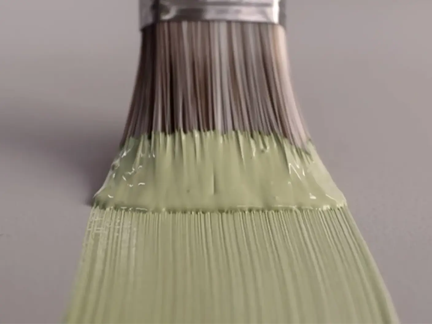 Pensel med ljusgrön färg stryker färgen över en grålila yta.