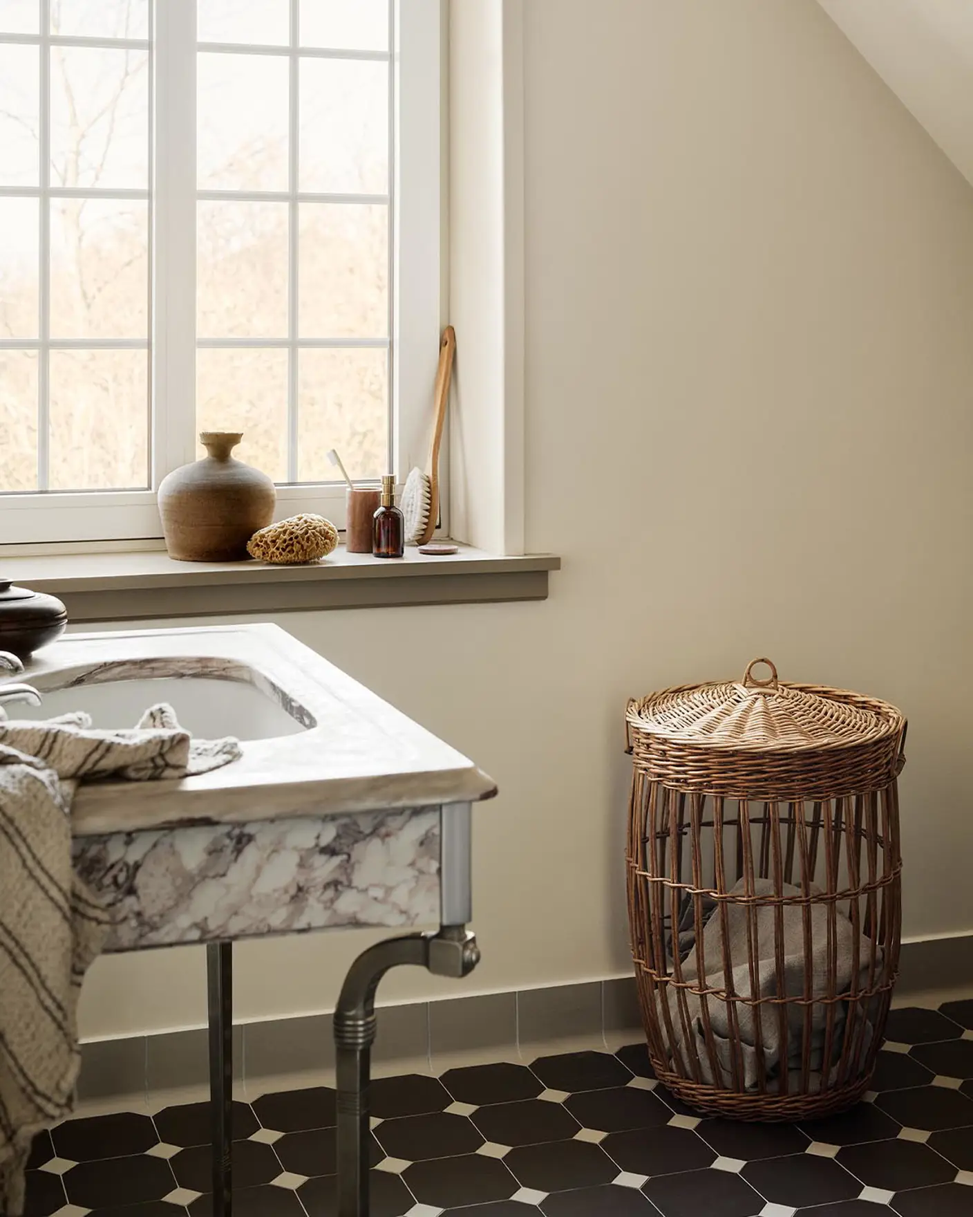 Bathroom with a marble sink, patterned floor tiles, and a wicker laundry basket against a wall painted with 12079 Gleam - a muted, greenish yellow colour from Jotun.
