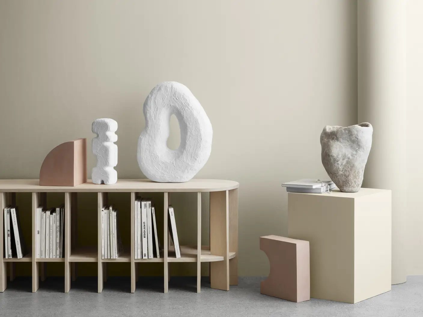 Minimalistisk interiør med skulpturelle dekorobjekter i naturmaterialer og lyse toner. Veggen er malt i en varm, beige nyanse som gir et rolig og harmonisk uttrykk, perfekt nøytral for moderne stue.