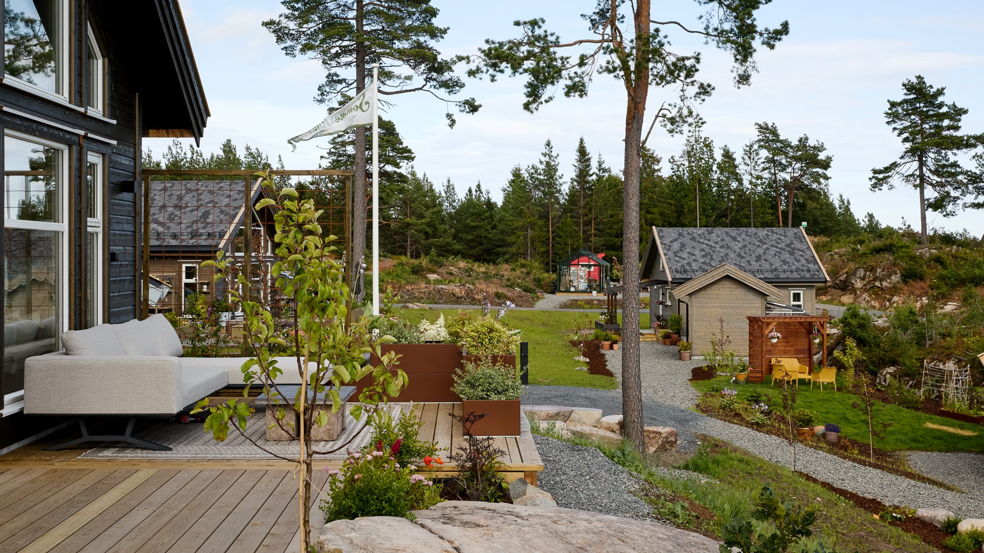 Moderne hytte med terrasse, hage og grussti i skogsområde i Norge