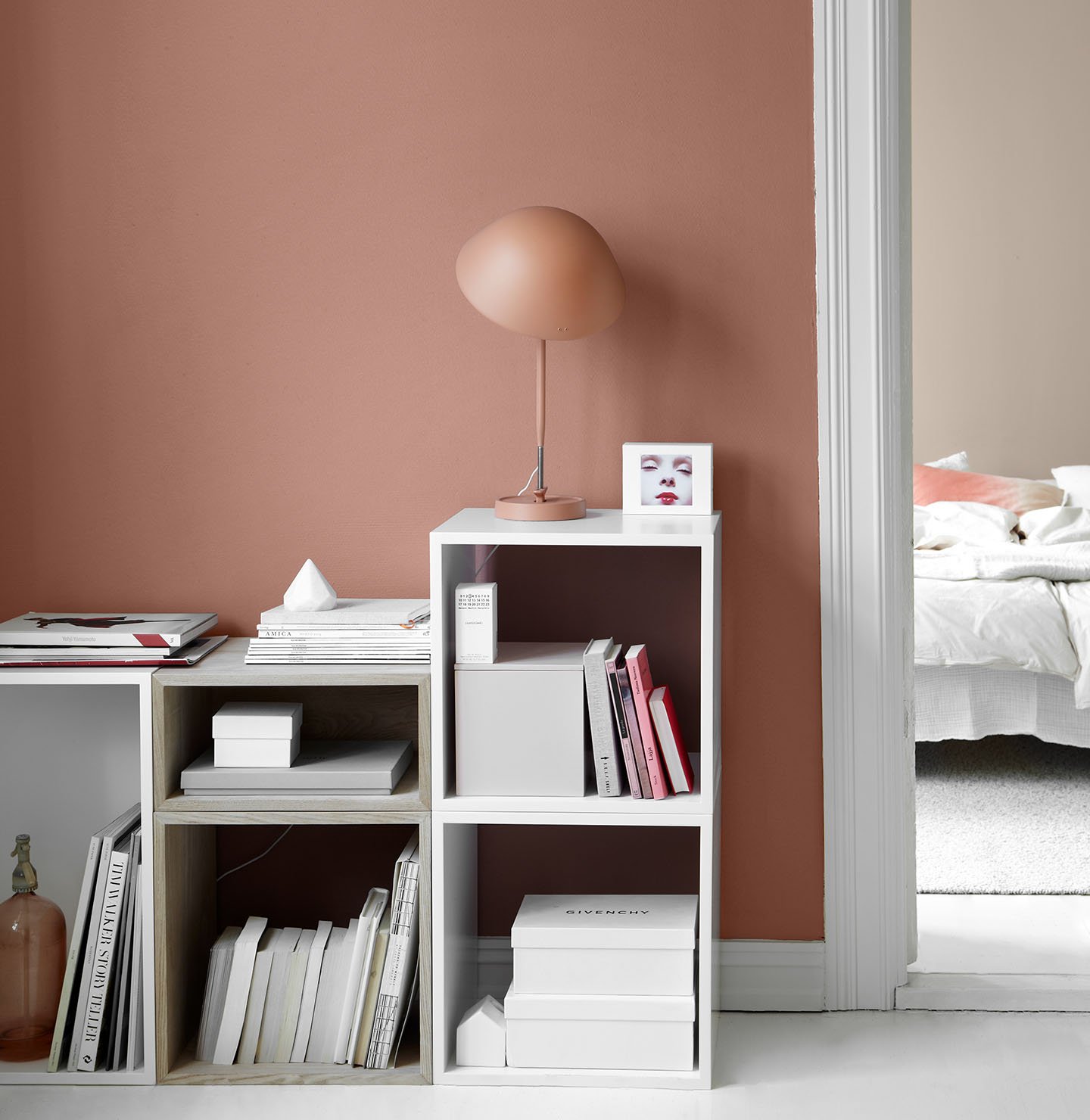 Modern interiör med en mjukt gyllenrosa vägg målad med Jotun 2856 Warm Blush, minimalistiska hyllor och en skulptural lampa, med en glimt in i ett dämpat gyllenrosa sovrum målat med Jotun 10580 Soft Skin.