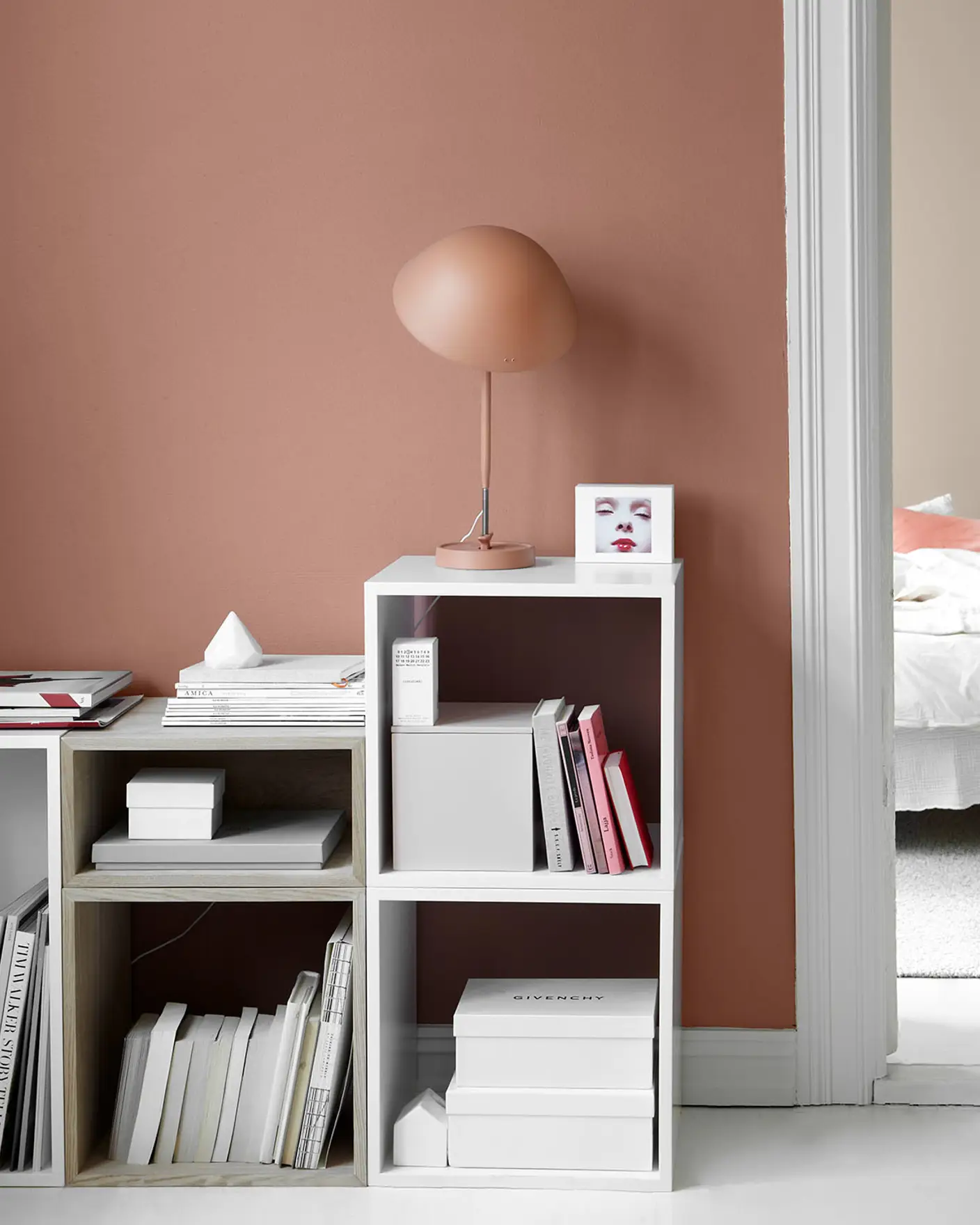 Modern interiör med en mjukt gyllenrosa vägg målad med Jotun 2856 Warm Blush, minimalistiska hyllor och en skulptural lampa, med en glimt in i ett dämpat gyllenrosa sovrum målat med Jotun 10580 Soft Skin.