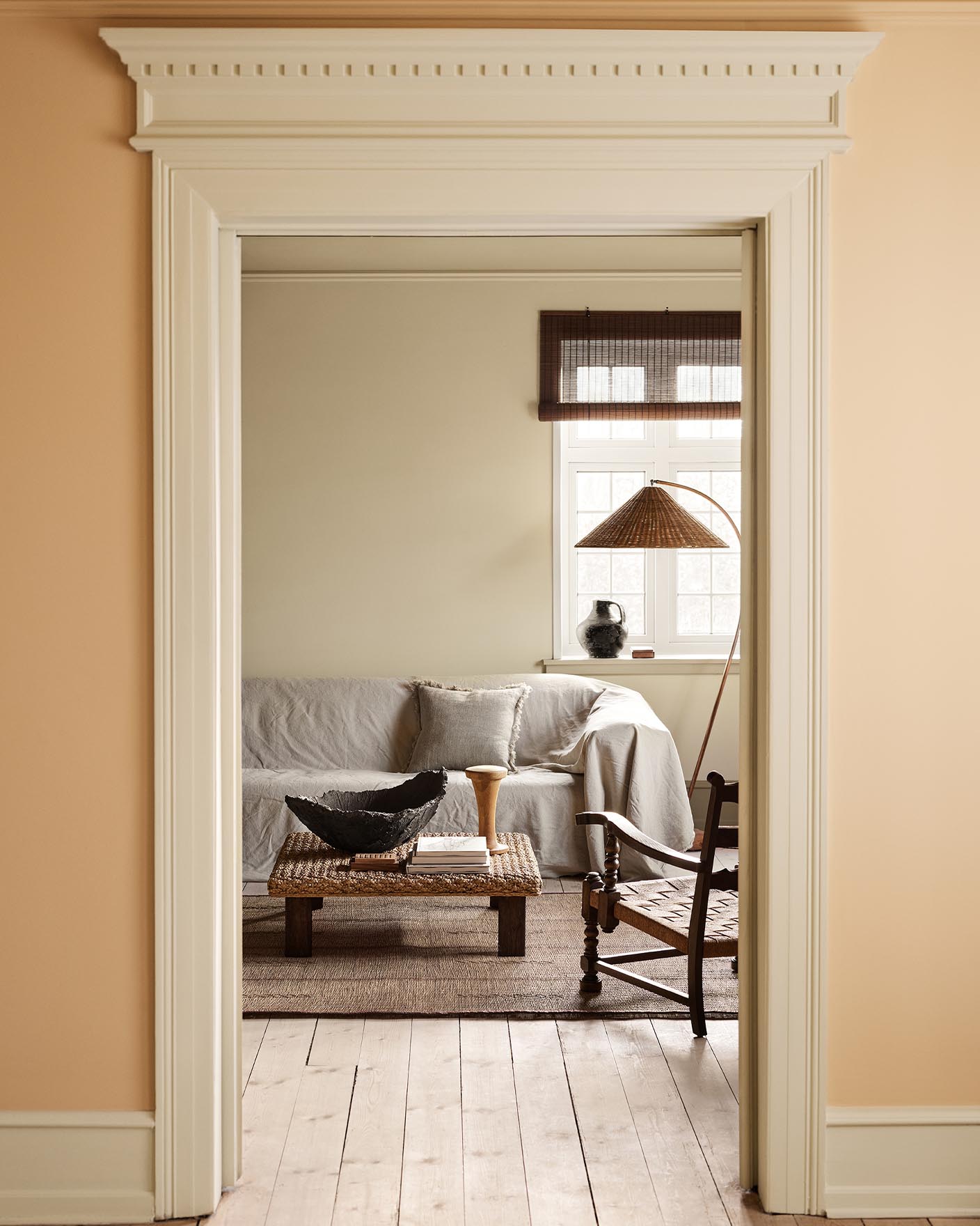 Living room with a light sofa, woven coffee table against a muted yellow wall painted in 12080 Soft Radiance. Wall in front in the colour 11202 Mild Ochre.