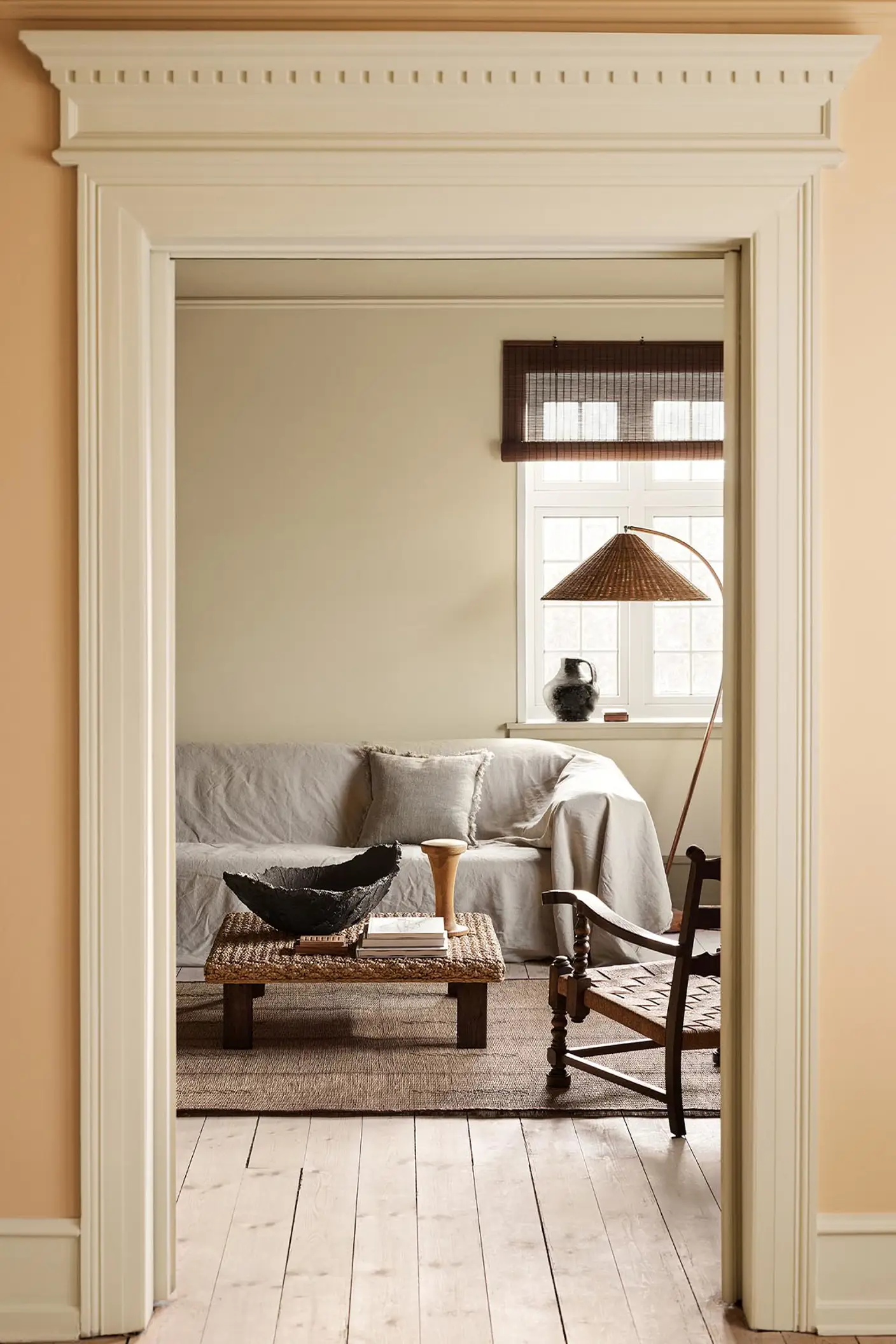 Living room with a light sofa, woven coffee table against a muted yellow wall painted in 12080 Soft Radiance. Wall in front in the colour 11202 Mild Ochre.