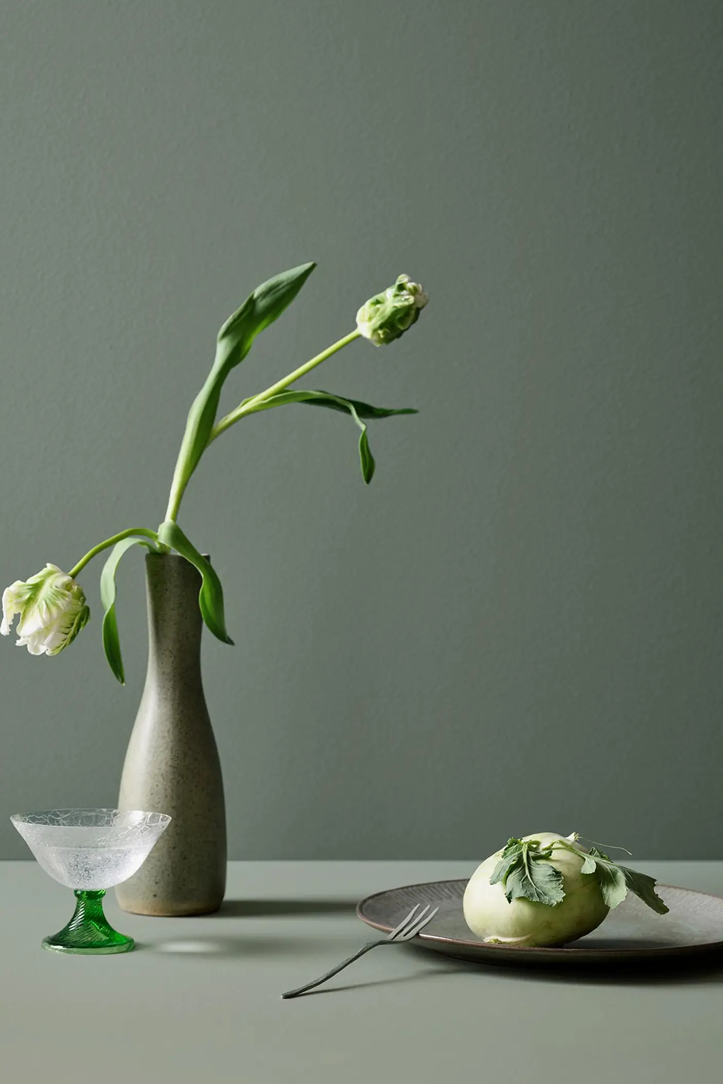 En tulpan i en vas på ett bord i mjuka gröna toner målat med Jotun 7685 Subtle Green, med en bakgrundsvägg målad i 7686 Mindful Green från Jotun.