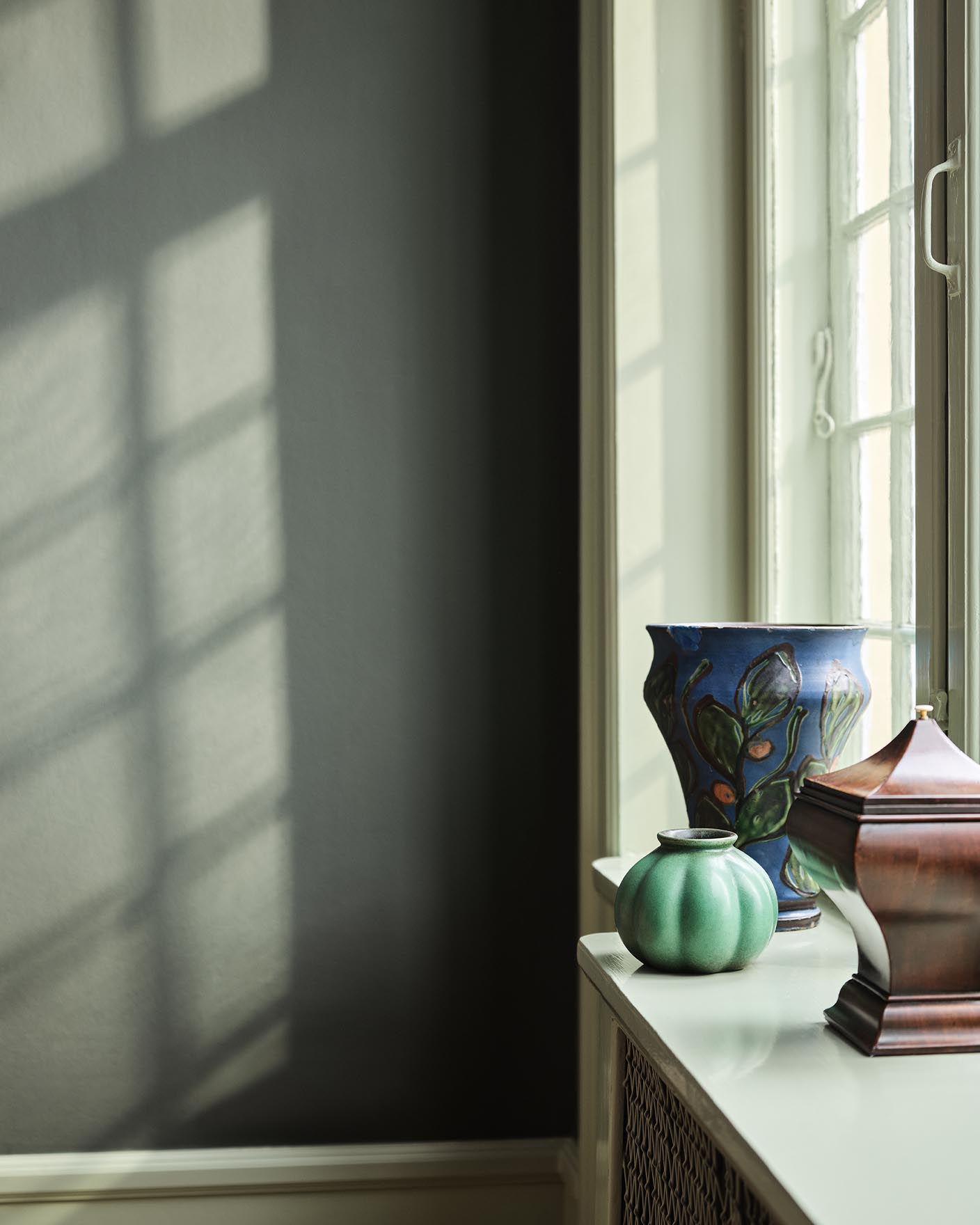 Green and blue vases standing in a window against a muted, dark green wall painted with the colour 7613 Northern Mystic from Jotun.