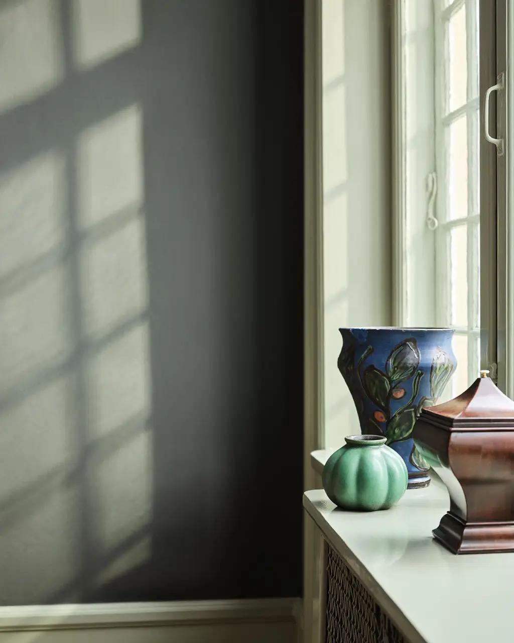 Green and blue vases standing in a window against a muted, dark green wall painted with the colour 7613 Northern Mystic from Jotun.