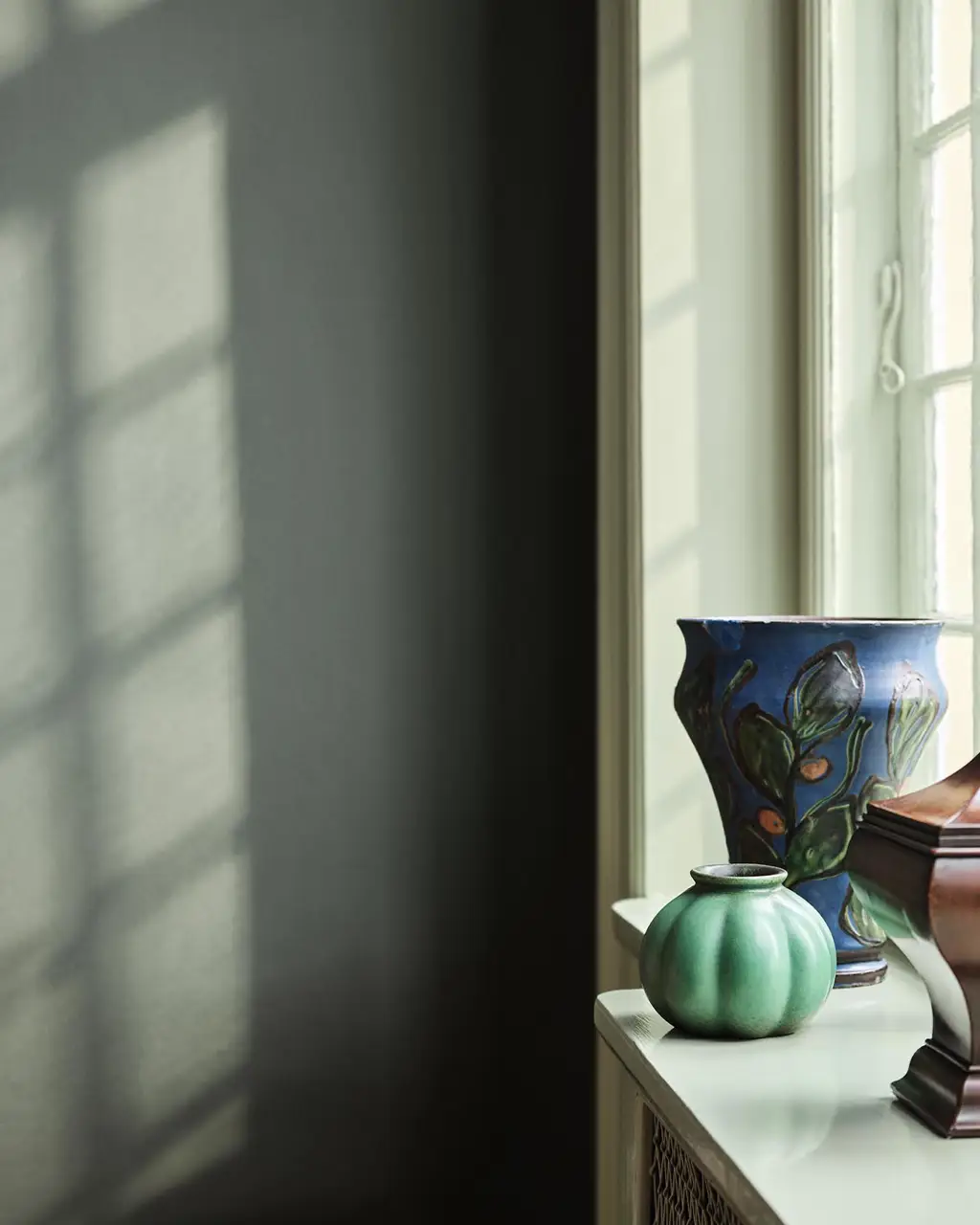 Green and blue vases standing in a window against a muted, dark green wall painted with the colour 7613 Northern Mystic from Jotun.