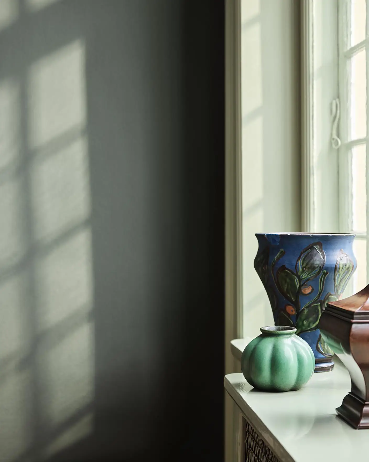 Green and blue vases standing in a window against a muted, dark green wall painted with the colour 7613 Northern Mystic from Jotun.
