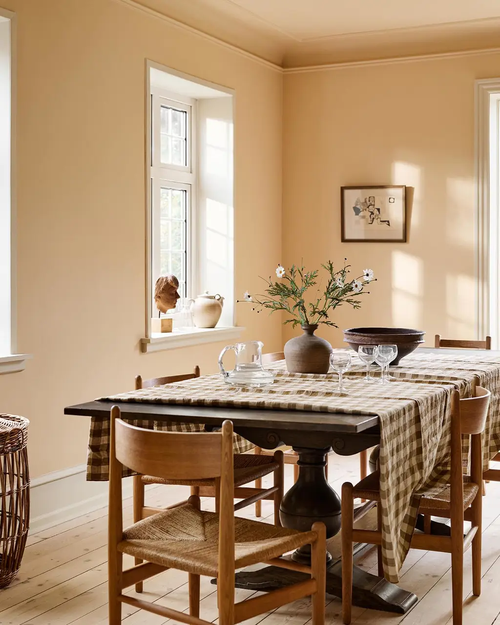 Dining room with a checkered tablecloth, wooden chairs, against an ochre yellow wall painted in the colour 11202 Mild Ochre from Jotun.