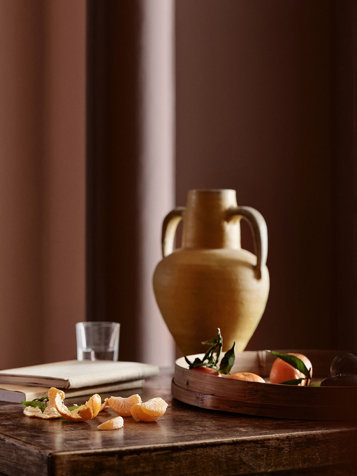 Et stilleben med citrusfrugter og en amforavase foran vægge malet i den røde nuance Jotun 20118 Amber Red samt en søjle malet i den brunrøde nuance Jotun 2993 Kilim.