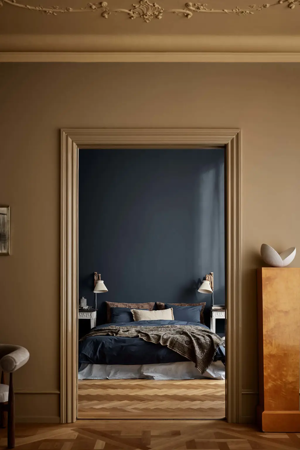 En stue med vægge i brun Jotun 1799 Spice Brown og loft i okkergul Jotun 1909 Kalkoker, med udsigt ind til et soveværelse med en dyb blå væg malet i Jotun 4403 Midnight Blue.