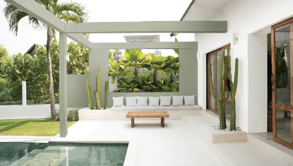 Modern white tropical villa with poolside lounge chairs, a white umbrella, and lush green palm trees